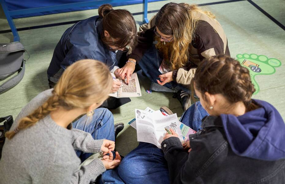 Vier Jugendliche sitzen in eim Kreis auf dem Boden und lesen in Informationsheften