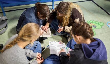 Vier Jugendliche sitzen in eim Kreis auf dem Boden und lesen in Informationsheften