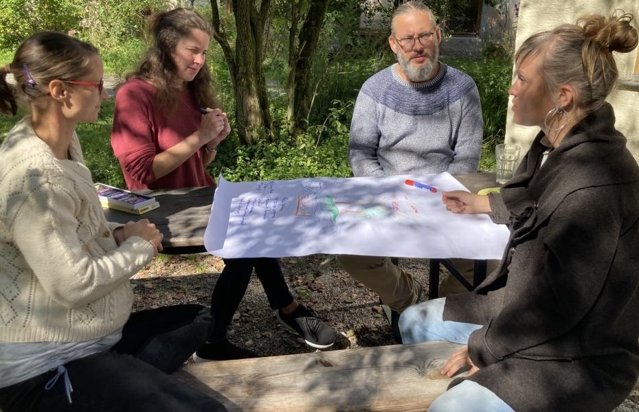 Vier Erwachsen sitzen im Garten an einem Tisch und erstellen ein Präsentation