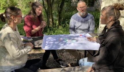 Vier Erwachsen sitzen im Garten an einem Tisch und erstellen ein Präsentation