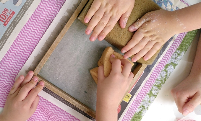 vier Kinderhände stellen selbst Papier her mit einen Schöpfrahmen