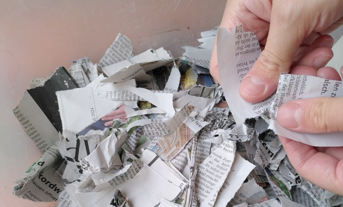 Hände zerreissen Zeitungspapier - ein kleiner Stapel zerrissenes Papier liegt bereits auf dem Tisch