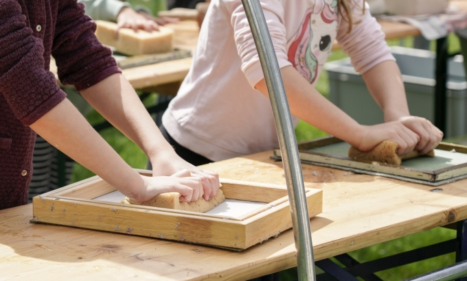 Hände und Arme von Kindern, die stehend an einem Tisch mit dem Papierschöpfrahmen arbeiten