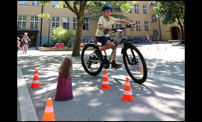 Kind auf dem Fahrrad umfährt Hindernisse, die auf einem Schulhof aufgebaut sind