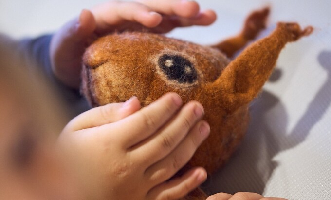 Kinderhände streicheln den Kopf eines Eichhörchens; diese Einhörnchen ist aus Filz gestaltet