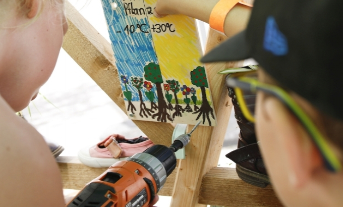  Zwei Kinder befestigen ein selbstgestaltetes Plakat an einen Informationsstand - das Plakat veranschaulicht die Wichtigkeit der Bäume hinsichtlich Umweltschutz